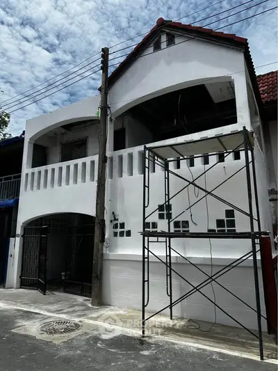 Charming two-story white house under renovation with scaffolding, showcasing potential for modern upgrades.