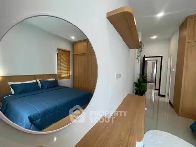 Modern bedroom with stylish wooden accents and round mirror reflecting cozy bed.