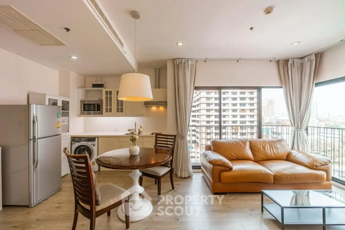 Modern open-plan living room with kitchen, featuring a cozy leather sofa and city view balcony.