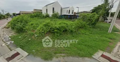 Vacant land with lush greenery and modern house in the background, ideal for development.