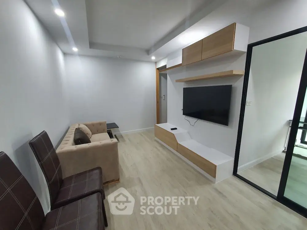 Modern living room with sleek TV setup and cozy seating in a bright apartment.