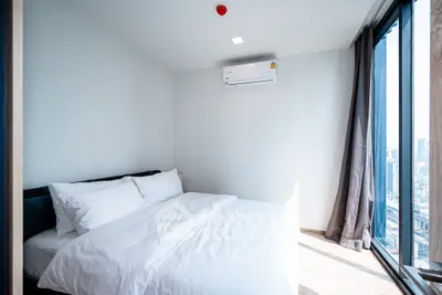 Modern bedroom with city view, featuring a cozy bed and large windows for natural light.