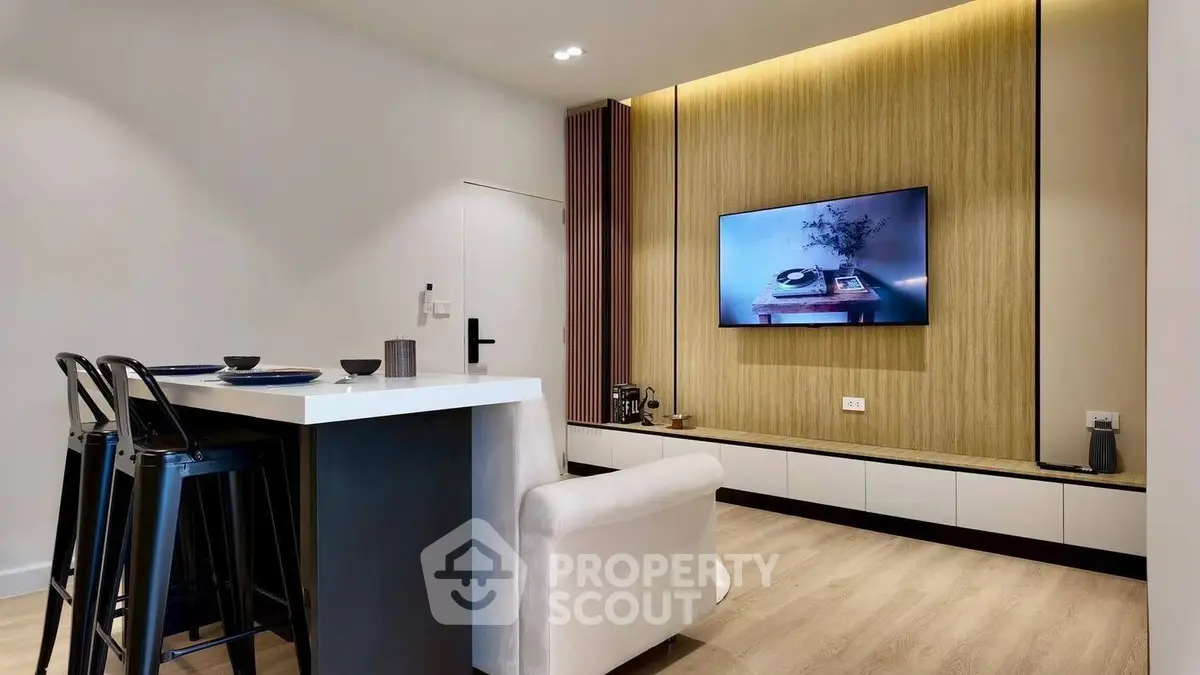 Modern living room with stylish decor and wall-mounted TV, featuring sleek furniture and warm lighting.