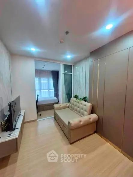 Modern living room with cozy sofa and TV, leading to a stylish bedroom with natural light.