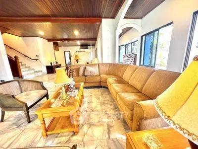 Spacious living room with elegant furniture and natural light, featuring a large curved sofa and marble flooring.