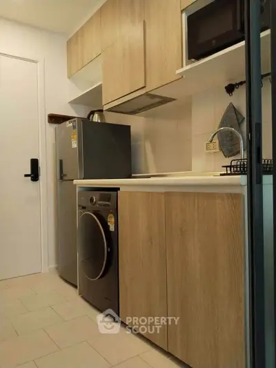 Modern kitchen with wooden cabinets, washing machine, and compact fridge in a cozy apartment.