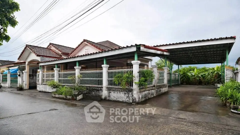 Charming single-story house with spacious carport and lush greenery, perfect for serene living.