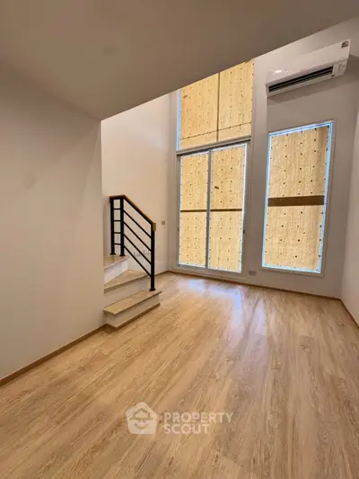 Spacious modern living room with high ceilings and large windows, featuring sleek wooden flooring and a stylish staircase.