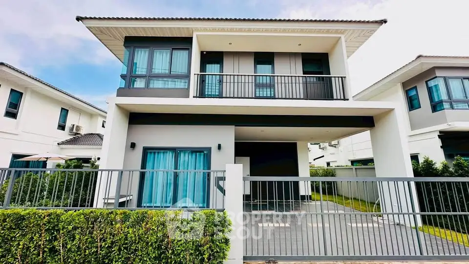 Modern two-story house with balcony and gated driveway in a suburban neighborhood.