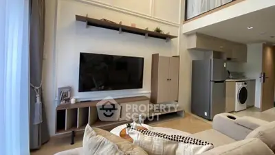 Modern living room with stylish furniture, TV, and open kitchen featuring fridge and washing machine.