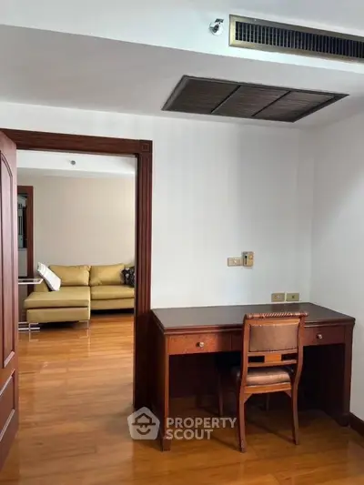 Spacious study area with wooden desk and chair, leading to cozy living room with sofa.