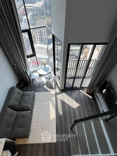 Stunning loft apartment with floor-to-ceiling windows and city view, featuring modern decor and cozy seating area.