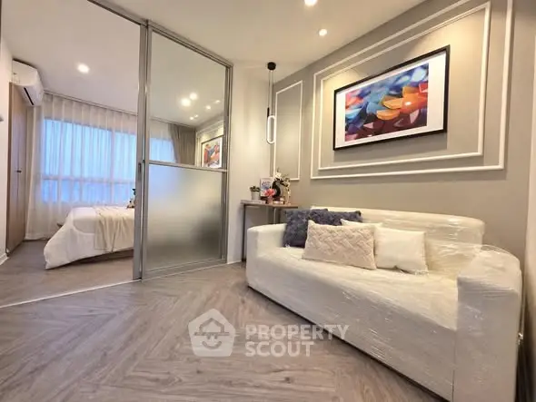 Modern apartment interior with stylish living room and cozy bedroom separated by glass partition.