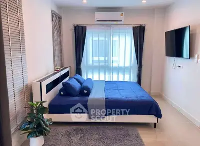 Modern bedroom with blue bedding, wall-mounted TV, and large window with curtains.