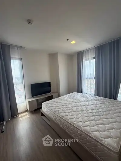 Spacious bedroom with large windows and natural light, featuring a modern bed and flat-screen TV.