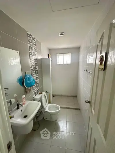 Compact bathroom with modern fixtures and tiled walls, featuring a shower area and small window for natural light.