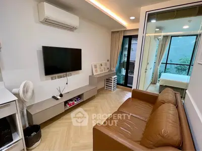 Modern living room with leather sofa and wall-mounted TV, leading to a bedroom with balcony view.