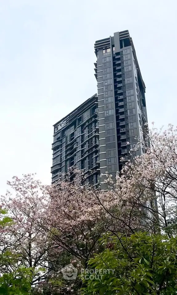 Modern high-rise building with sleek design surrounded by blooming trees, offering urban living with nature views.