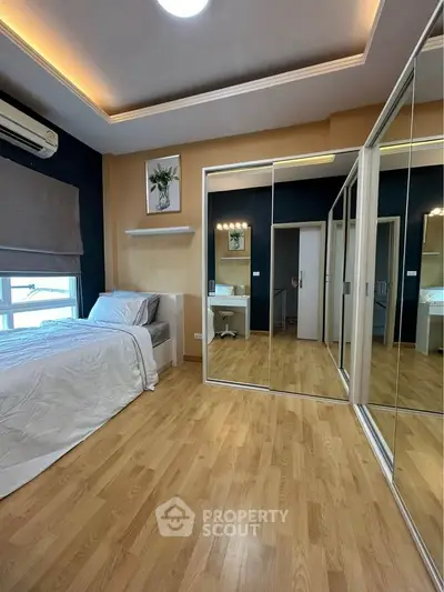 Modern bedroom with mirrored closet doors and wooden flooring, featuring a cozy bed and stylish decor.