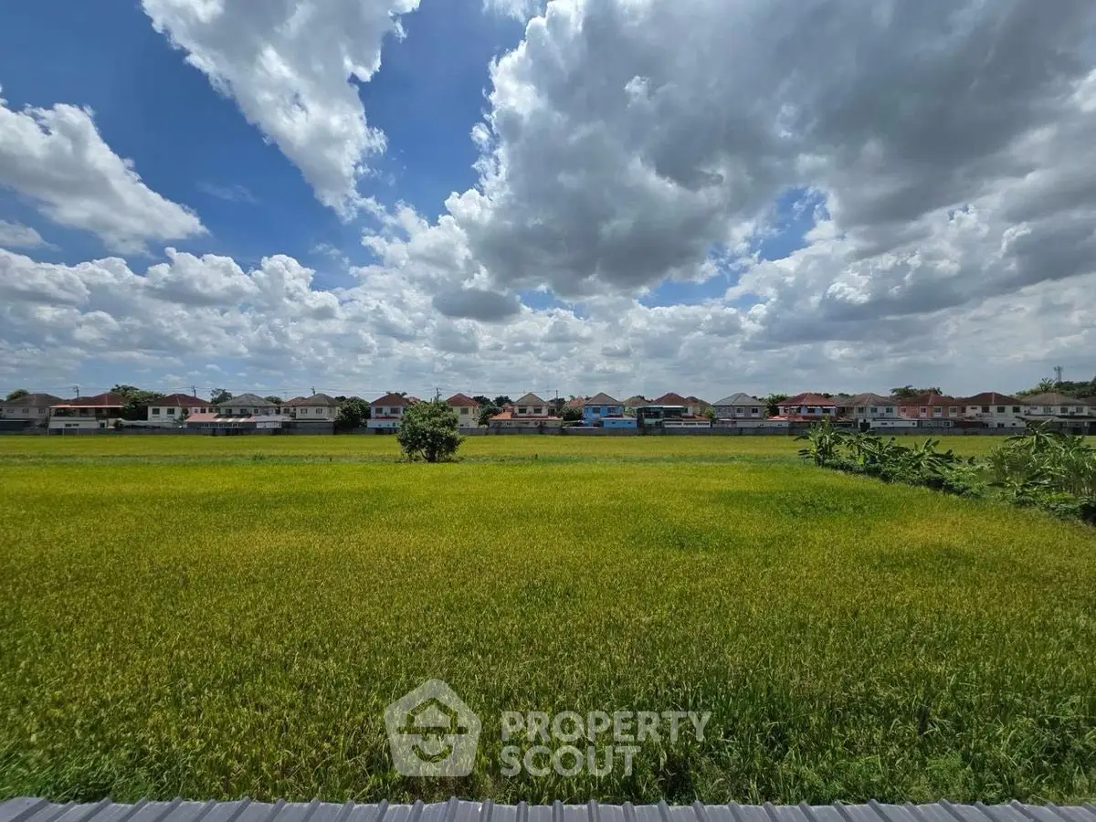 Scenic view of lush green fields with suburban houses under a vibrant sky.