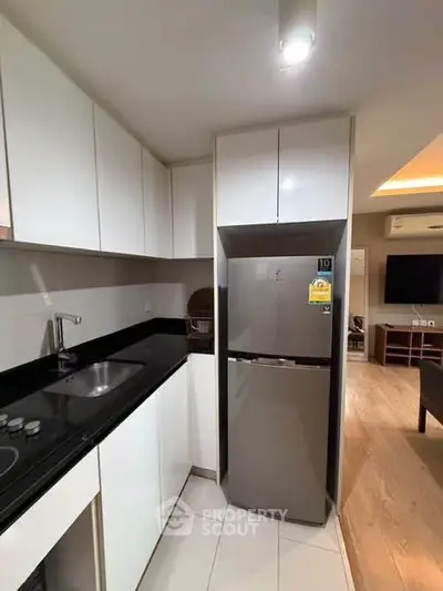Modern kitchen with sleek white cabinets and stainless steel fridge in a stylish apartment.
