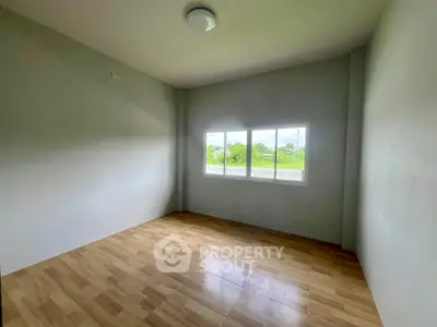 Spacious empty room with large window and wooden flooring, ideal for customization.