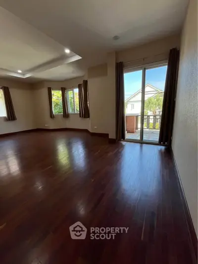 Spacious living room with hardwood floors and large windows offering natural light and garden view.