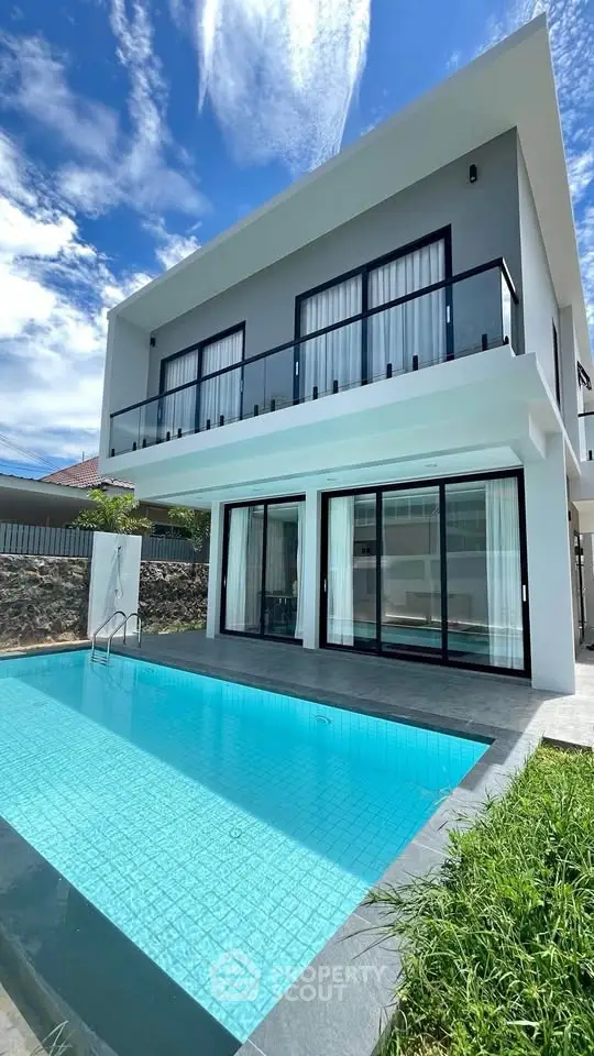 Modern two-story house with pool and large windows under a clear blue sky.