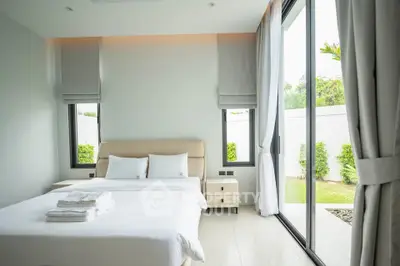 Bright and modern bedroom with large windows overlooking a garden, featuring a cozy bed and minimalist decor.