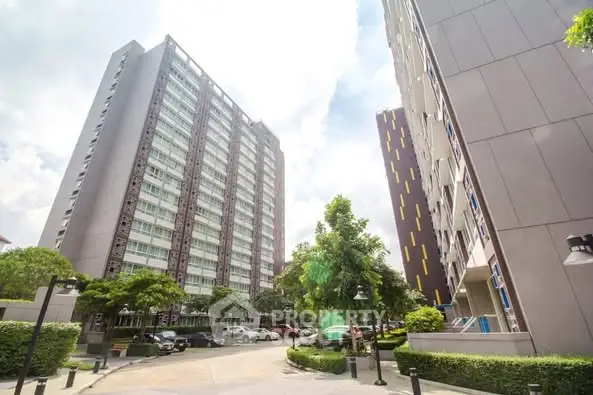Modern high-rise apartment buildings with lush greenery and parking area.