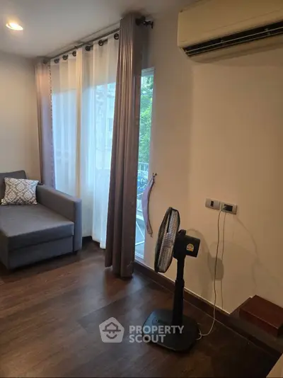 Cozy living room with modern sofa, air conditioning, and floor fan, featuring elegant curtains and wooden flooring.