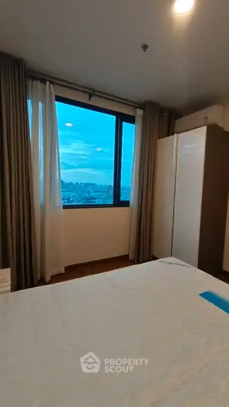 Spacious bedroom with large window offering stunning city views, perfect for relaxation and comfort.