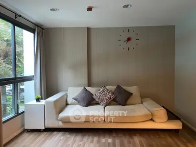 Stylish living room with modern sofa and wall clock, featuring large window with garden view.
