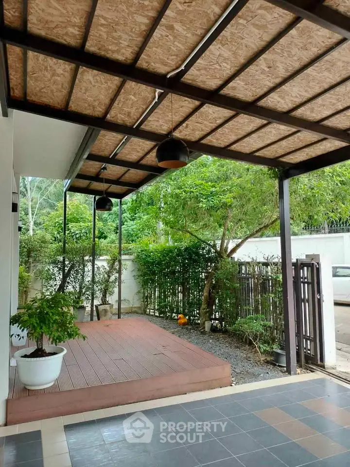 Charming covered patio with wooden deck and lush greenery, perfect for outdoor relaxation.