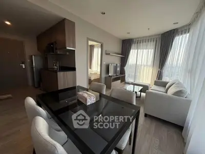 Modern open-plan living room with dining area and kitchen, featuring large windows and stylish decor.