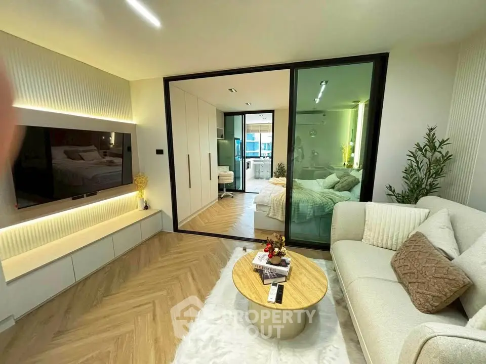 Modern living room with cozy decor and view into a stylish bedroom, featuring elegant furniture and warm lighting.