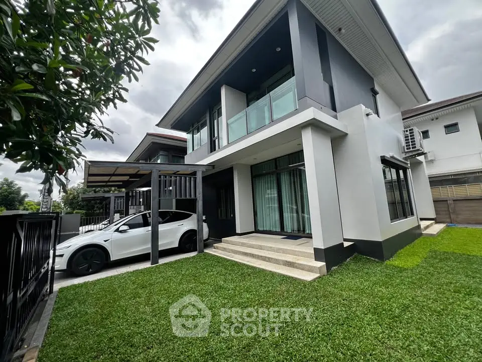 Modern two-story house with sleek design and spacious lawn, featuring a carport and large windows for natural light.