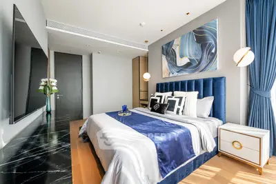 Luxurious modern bedroom with elegant decor and large TV, featuring blue accents and stylish artwork.