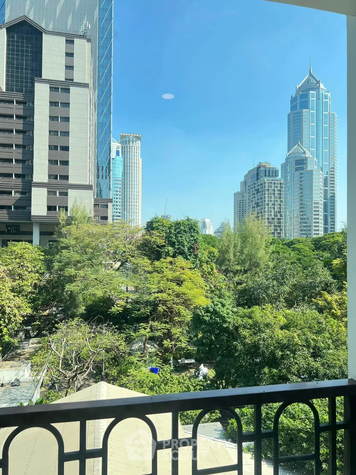 Stunning cityscape view from a balcony overlooking lush greenery and modern skyscrapers.