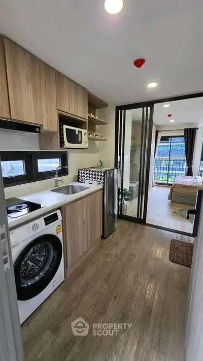 Modern apartment kitchen with washing machine and sliding glass doors leading to a bedroom with balcony view.
