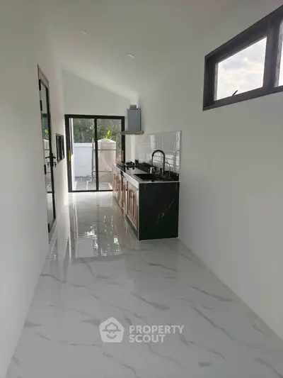 Sleek modern kitchen with marble flooring and open layout leading to outdoor space.