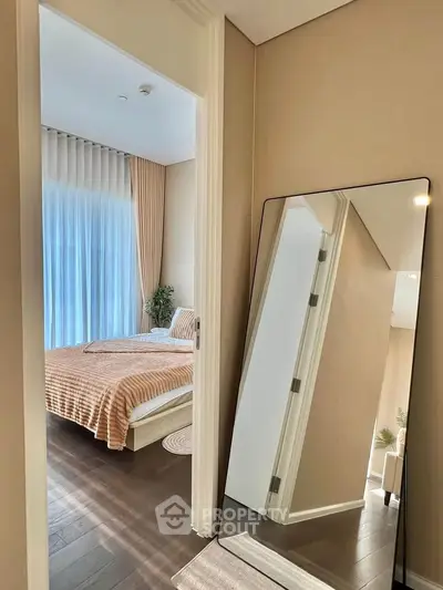Modern bedroom with elegant decor and full-length mirror, showcasing natural light and cozy ambiance.