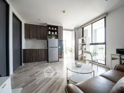 Modern living room with open kitchen and balcony view, featuring sleek furniture and natural light.