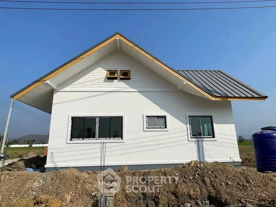 Charming single-story house with modern roof and large windows in a serene countryside setting.