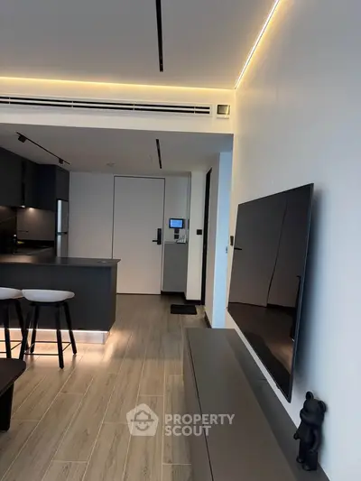 Modern living room with sleek design, featuring a wall-mounted TV and stylish kitchen area.