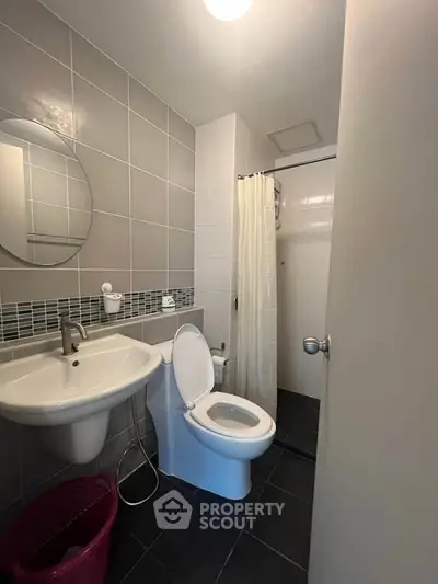 Modern bathroom with sleek fixtures, round mirror, and tiled walls, offering a clean and contemporary design.