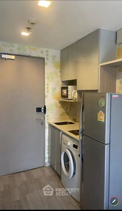 Compact modern kitchen with stainless steel appliances and washing machine in a cozy apartment.