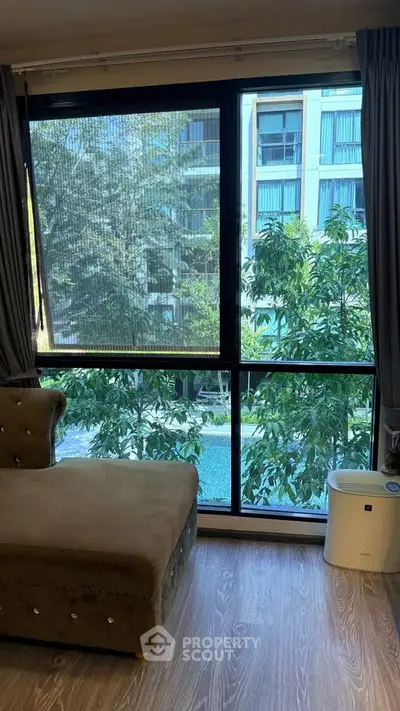 Spacious living room with large window offering lush garden and pool view, perfect for relaxation.