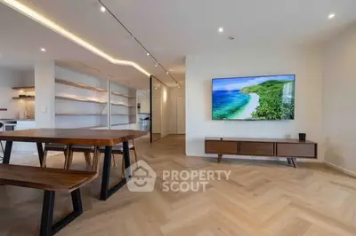 Spacious modern living room with wooden flooring and large wall-mounted TV, open to kitchen area.