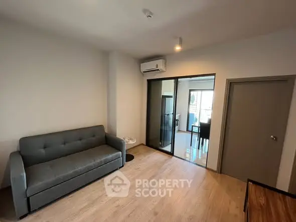 Modern living room with sleek sofa and air conditioning, featuring a sliding glass door to dining area.